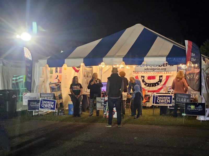 Vendor tent at night with signs for Democratic candidates in 2025