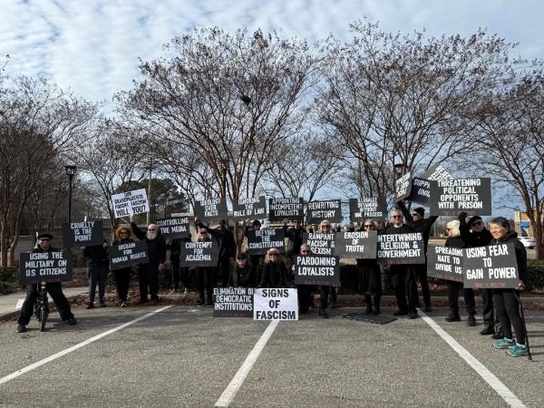 People dressed in black with "Signs of Fascism" signs.  Ex